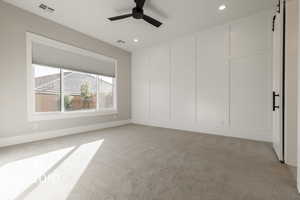 Carpeted spare room featuring ceiling fan and a barn door