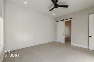 Unfurnished bedroom featuring connected bathroom, a barn door, ceiling fan, and light colored carpet