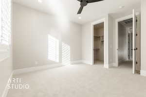 Unfurnished bedroom featuring a closet, light colored carpet, a spacious closet, and ceiling fan