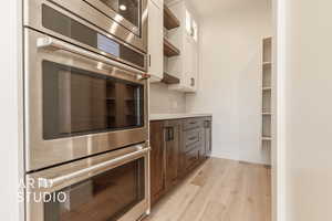 Kitchen with appliances with stainless steel finishes, backsplash, dark brown cabinetry, light hardwood / wood-style flooring, and white cabinets