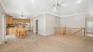 Kitchen featuring white appliances, light colored carpet, crown molding, pendant lighting, and a center island