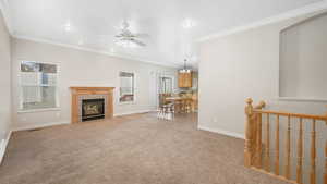 Unfurnished living room with a tile fireplace, light carpet, ceiling fan, and ornamental molding