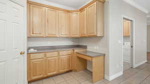 Kitchen featuring light brown cabinetry, washer / clothes dryer, light tile patterned floors, and crown molding