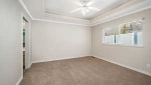 Carpeted empty room with a tray ceiling, crown molding, and ceiling fan