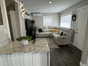 Living room with a textured ceiling, dark hardwood / wood-style floors, and a wall mounted AC