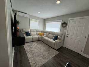 Living room featuring an AC wall unit, dark hardwood / wood-style flooring, and a textured ceiling