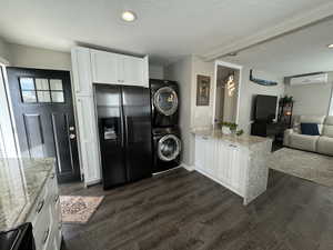 Kitchen featuring kitchen peninsula, stacked washer and dryer, dark hardwood / wood-style floors, black fridge with ice dispenser, and white cabinetry