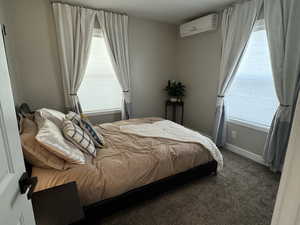 Bedroom featuring a wall unit AC, multiple windows, and dark colored carpet