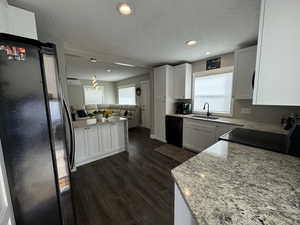 Kitchen with dark wood-type flooring, sink, black appliances, white cabinets, and hanging light fixtures