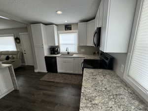 Kitchen with dark wood-type flooring, black appliances, white cabinets, sink, and a textured ceiling