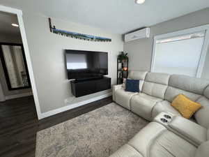 Living room with a wall unit AC, dark hardwood / wood-style flooring, and a textured ceiling