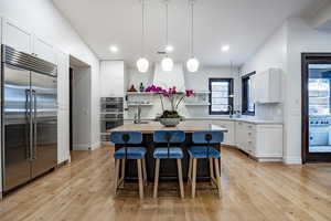 Kitchen featuring appliances with stainless steel finishes, light wood-type flooring, pendant lighting, a center island with sink, and white cabinetry