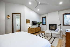 Bedroom featuring ceiling fan, a fireplace, connected bathroom, light hardwood / wood-style floors, and lofted ceiling