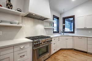 Kitchen featuring custom exhaust hood, high end stainless steel range oven, sink, light hardwood / wood-style floors, and white cabinetry