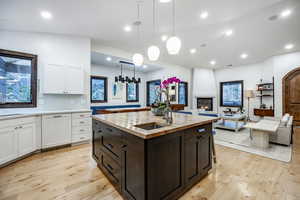 Kitchen featuring white cabinets, pendant lighting, light wood-type flooring, and a kitchen island with sink