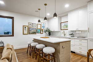 Kitchen with a center island, light hardwood / wood-style floors, white cabinetry, and pendant lighting