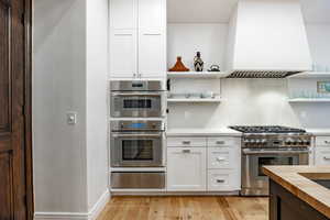 Kitchen featuring white cabinets, custom range hood, and appliances with stainless steel finishes