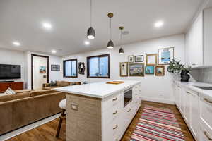 Kitchen with pendant lighting, a kitchen breakfast bar, dark hardwood / wood-style flooring, and white cabinetry