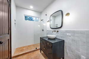 Bathroom with tile patterned floors, tiled shower, tile walls, and vanity