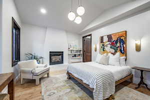 Bedroom with a fireplace, wood-type flooring, lofted ceiling, and a notable chandelier