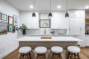 Kitchen with pendant lighting, sink, light wood-type flooring, a kitchen island, and white cabinetry