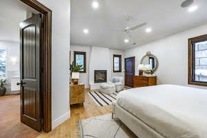 Bedroom featuring multiple windows, ceiling fan, a large fireplace, and light wood-type flooring