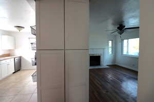 Kitchen featuring stainless steel dishwasher, a fireplace, ceiling fan, light hardwood / wood-style flooring, and white cabinets