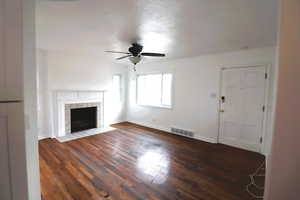 Unfurnished living room featuring dark hardwood / wood-style floors, ceiling fan, and a tiled fireplace