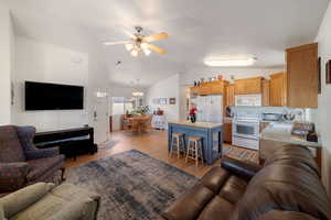 Living room with ceiling fan with notable chandelier, lofted ceiling, sink, and light hardwood / wood-style flooring