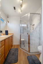 Bathroom featuring toilet, vanity, an enclosed shower, and hardwood / wood-style flooring