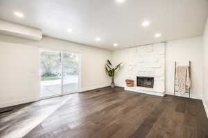 Unfurnished living room with a textured ceiling, dark hardwood / wood-style floors, and a stone fireplace