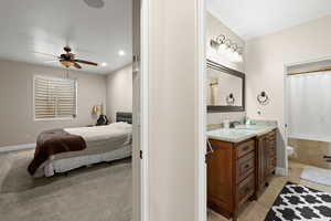 Bedroom with connected bathroom, ceiling fan, sink, and light colored carpet