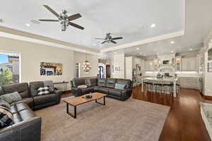 Living room featuring ceiling fan with notable chandelier, dark hardwood / wood-style flooring, a textured ceiling, and a tray ceiling