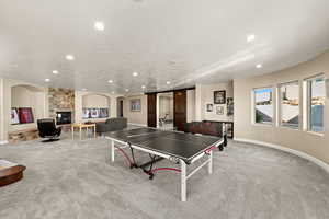 Game room featuring a textured ceiling, light colored carpet, and a stone fireplace