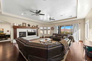 Living room with a textured ceiling, a tray ceiling, ceiling fan, and dark wood-type flooring