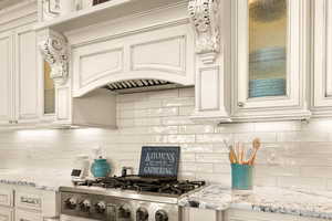 Kitchen featuring decorative backsplash, light stone counters, custom exhaust hood, stainless steel gas cooktop, and cream cabinetry