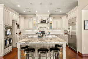 Kitchen with hanging light fixtures, appliances with stainless steel finishes, dark hardwood / wood-style flooring, and a kitchen island with sink