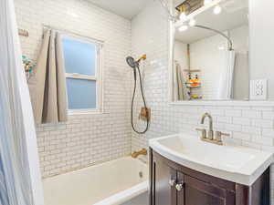 Bathroom with decorative backsplash, shower / bath combo, vanity, and tile walls