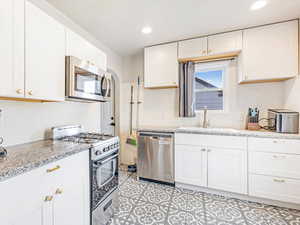 Kitchen featuring white cabinets, sink, light stone countertops, and stainless steel appliances