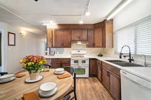 Kitchen with white appliances, light hardwood / wood-style floors, backsplash, and sink