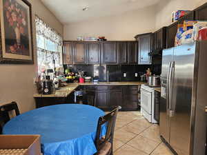 Kitchen with white gas range, stainless steel fridge with ice dispenser, backsplash, vaulted ceiling, and dark brown cabinets