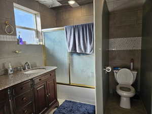 Full bathroom featuring vanity, tile patterned floors, bath / shower combo with glass door, toilet, and tile walls