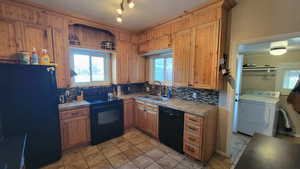 Kitchen featuring sink, tile counters, washer / dryer, decorative backsplash, and black appliances