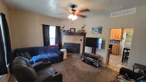 Living room with light carpet, a textured ceiling, ceiling fan, washer / dryer, and a tiled fireplace