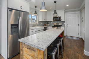 Kitchen featuring decorative light fixtures, stainless steel appliances, a kitchen island, and white cabinetry