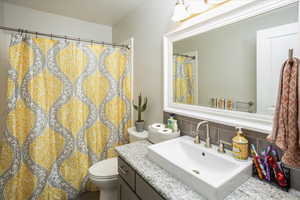 Bathroom featuring decorative backsplash, toilet, and vanity