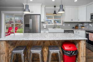 Kitchen featuring white cabinets, sink, appliances with stainless steel finishes, a kitchen island, and a kitchen bar