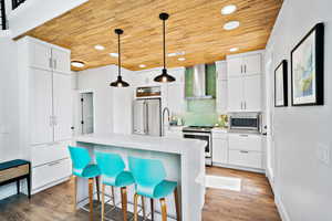 Kitchen with dark hardwood / wood-style flooring, wall chimney exhaust hood, stainless steel appliances, a center island, and hanging light fixtures