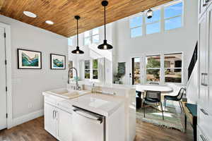 Kitchen featuring white cabinetry, light stone countertops, sink, stainless steel dishwasher, and decorative light fixtures