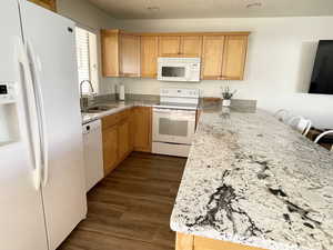 Kitchen with white appliances, sink, dark LVP flooring, a kitchen bar, and kitchen peninsula